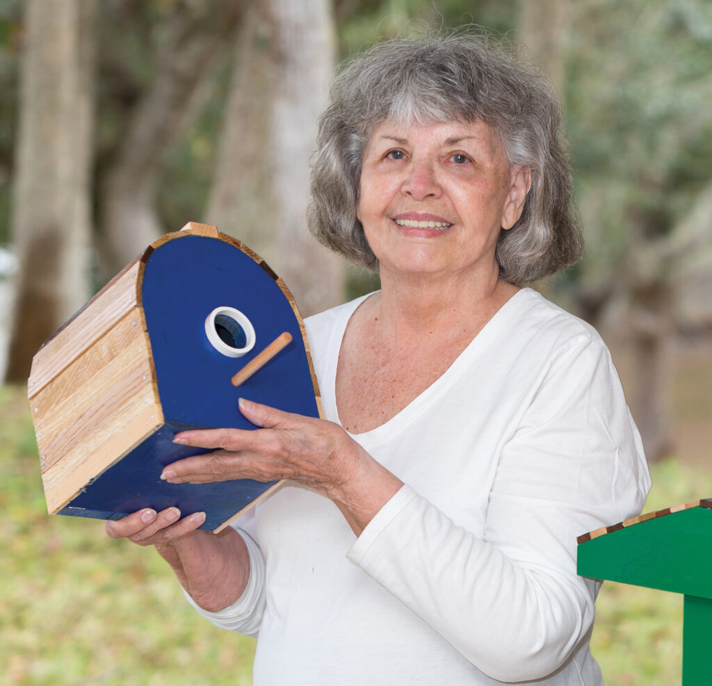 Robin Black on her patio holding a blue birdhouse and smiling.